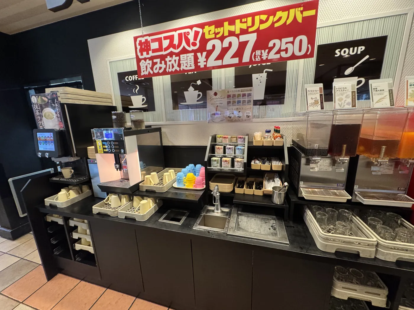 Gusto 的饮料吧。咖啡机、红茶包、果汁机、玻璃杯和杯子排成一排,上方挂着套餐饮料吧的价格牌。