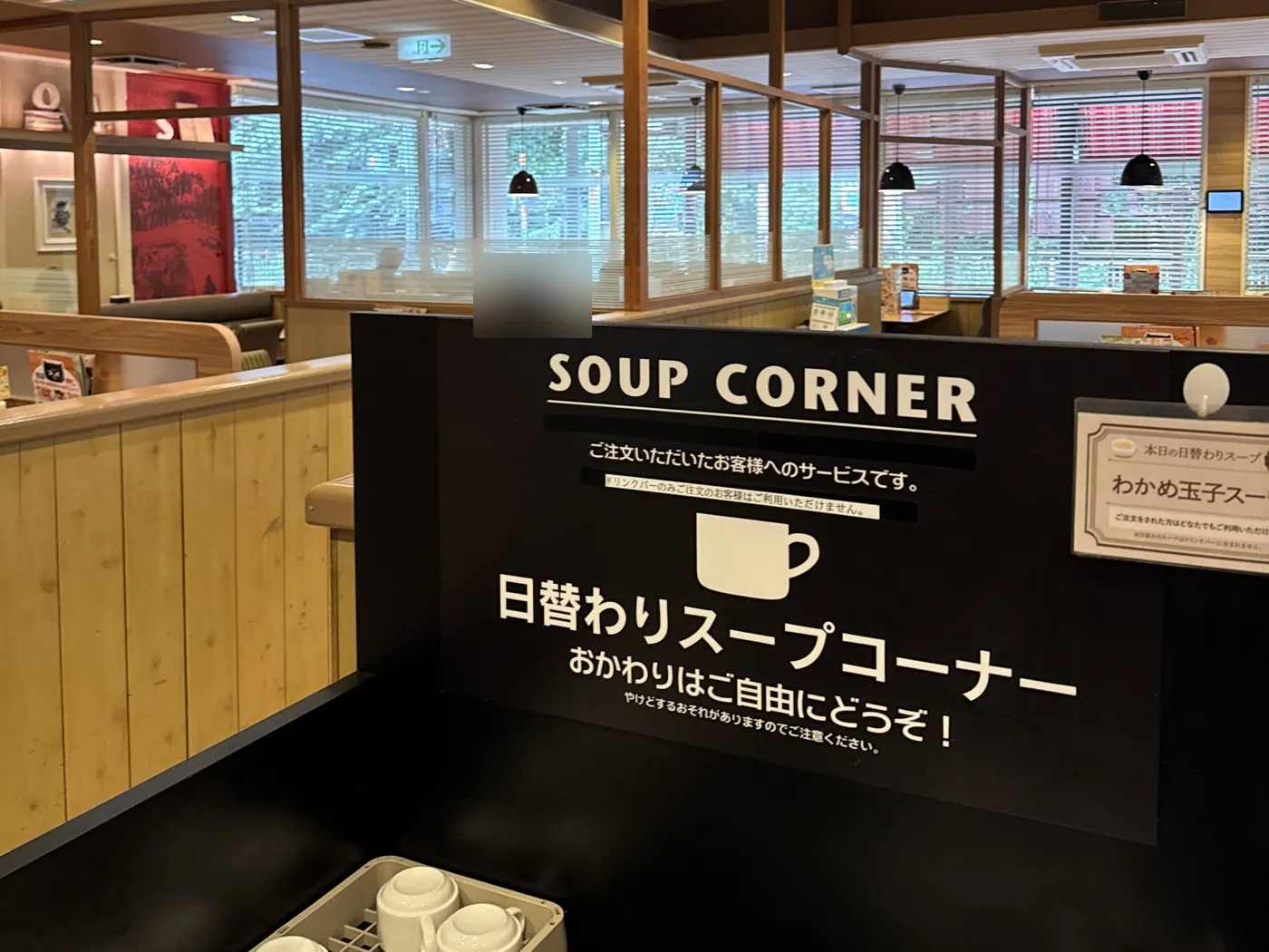 Gusto 的汤品区。黑色展板上有“SOUP CORNER”和日语说明,前面摆着盛汤用的杯子,后面是用餐区。