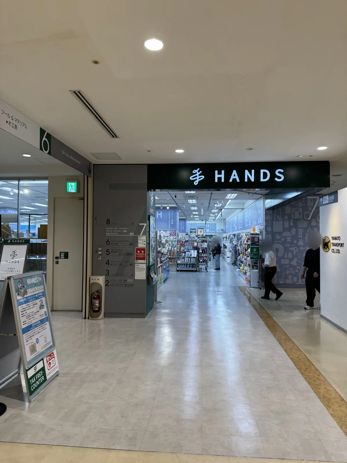L'ingresso dei reparti di HANDS al 7F. Un'insegna verde porta la scritta bianca “HANDS”, e sulla colonna a sinistra c'è la guida ai reparti di ogni piano, dall'8F al 2F. In basso sul cartello in primo piano c'è scritto “5F TAX FREE COUNTER”.