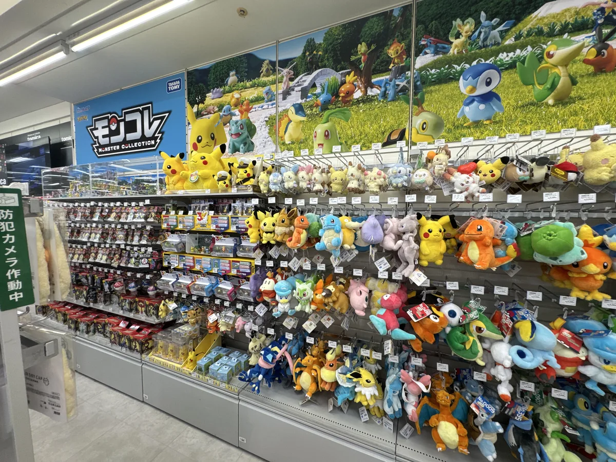 Molti peluche dei Pokémon appesi agli scaffali a parete. Sullo scaffale a sinistra sono allineate scatole di piccole figure dei Pokémon.