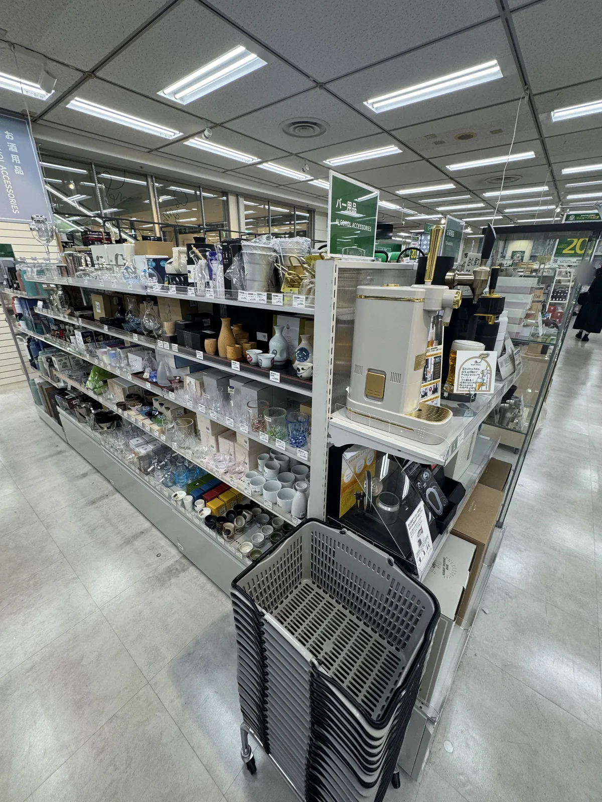 Uno scaffale di servizi per il sake. Ci sono caraffe tokkuri, coppette ochoko, bicchieri per il sake e altro; in alto c'è un cartellino con la scritta “バー用品” (articoli da bar).