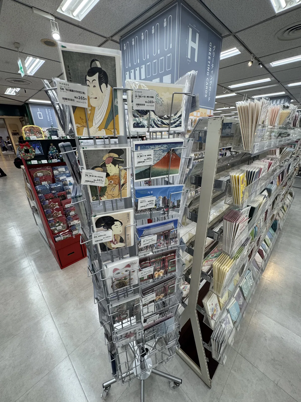 Su un espositore girevole ci sono cartoline con stampe ukiyo-e che raffigurano attori, donne, il monte Fuji e onde, e ogni tipo ha il suo cartellino del prezzo.