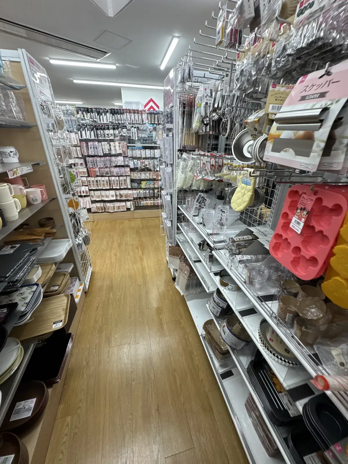 Pasilyo ng seksyon ng mga gamit sa kusina sa DAISO. Sa kanang istante ay may mga kagamitan sa pagluluto, hulmahan para sa pastry, at paper cup; sa kaliwa ay may mga kahoy na tray at plato.