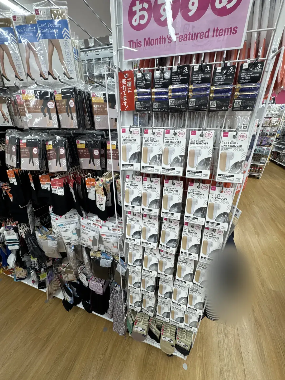 Display na may nakasulat na "おすすめ This Month's Featured Items". May mga baterya at lint remover na may markang 200 yen.