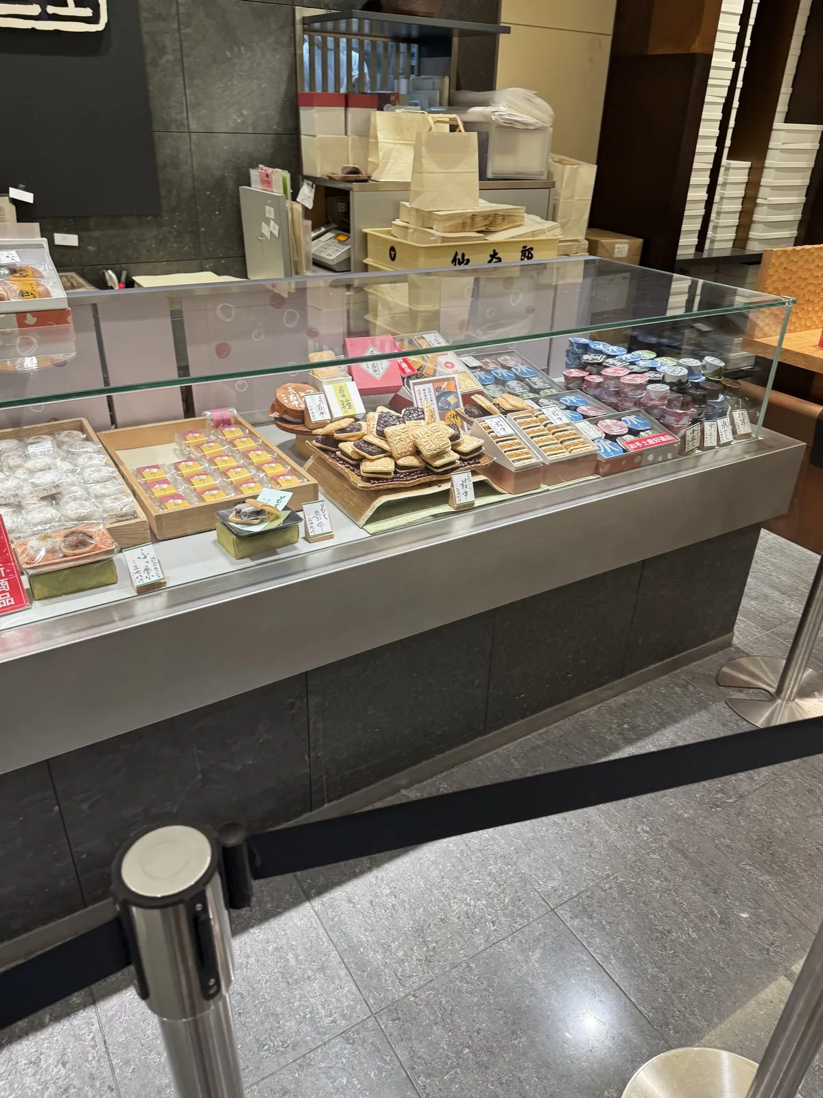 ตู้โชว์ของร้านขนมญี่ปุ่นชั้น B1F ของอาคารหลัก มีขนมบรรจุกล่องเรียงอยู่ แต่ละกล่องมีป้ายราคาติดอยู่