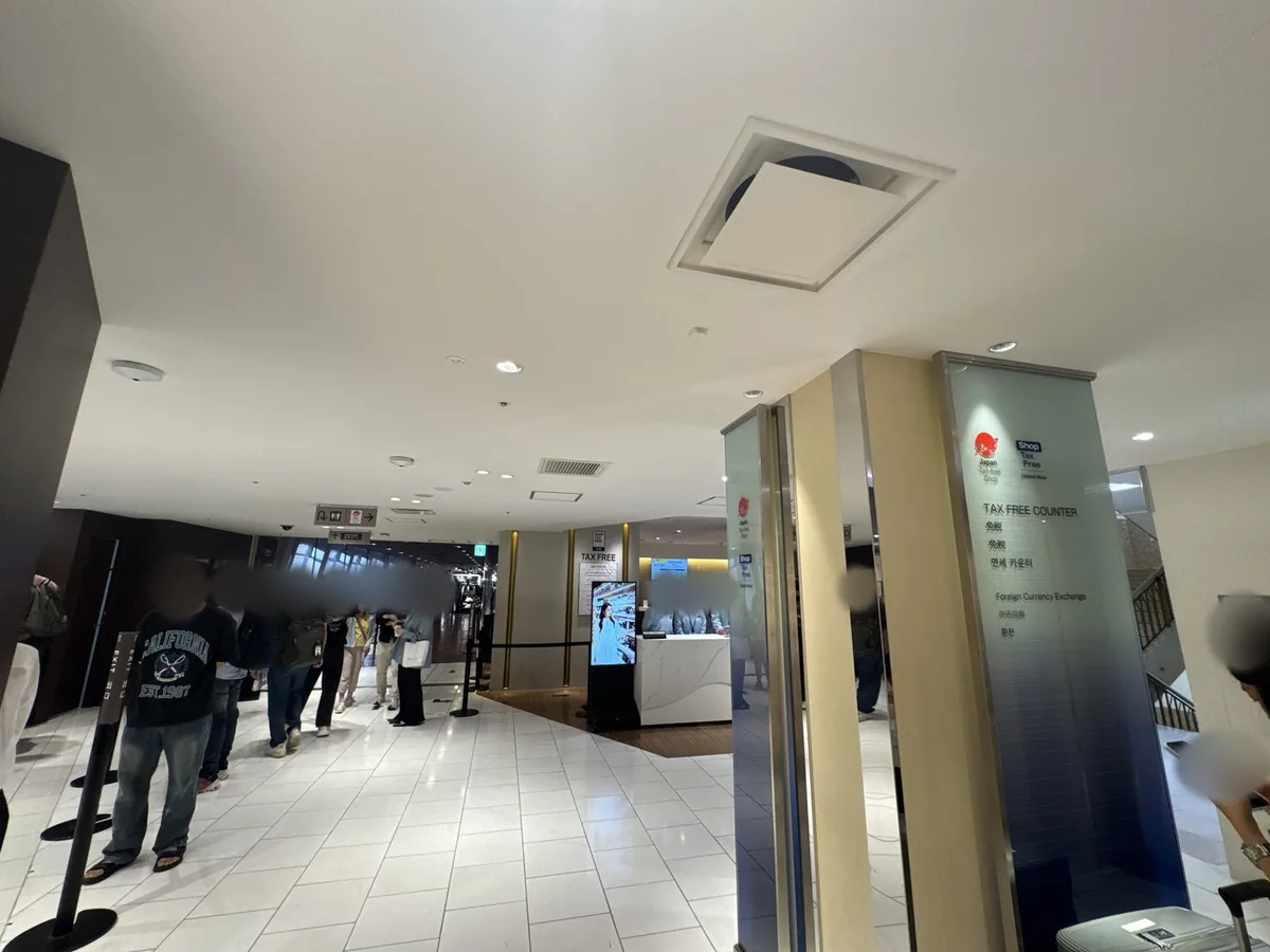 หน้าเคาน์เตอร์ปลอดภาษีชั้น 6F ของอาคารหลัก ป้ายแนะนำที่เสาเขียนว่า "TAX FREE COUNTER" พร้อมคำว่า "免税" "免税" "면세 카운터" ในภาษาญี่ปุ่น จีนตัวย่อ และเกาหลี ด้านล่างเขียนว่า "Foreign Currency Exchange" ด้านในมีเคาน์เตอร์สีขาวและเสากั้นแถว