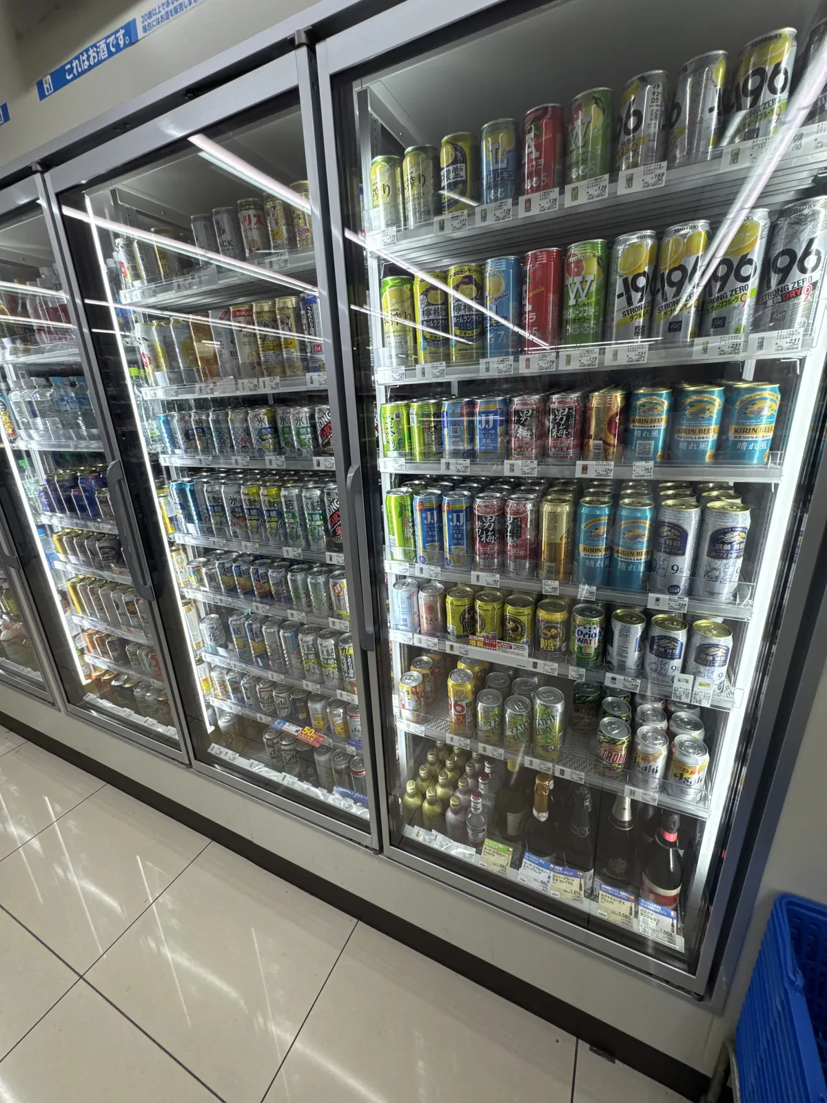 Pintu peti sejuk di Lawson. Bir, chuhai dan highball dalam tin serta minuman beralkohol dalam botol disusun, dan di atasnya terdapat tanda "これはお酒です" (Ini minuman beralkohol).