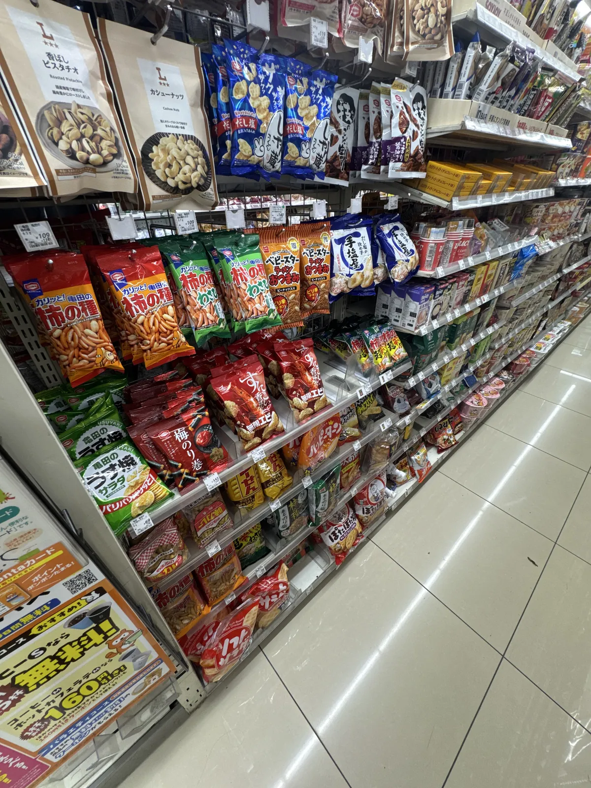 Rak snek di Lawson. Kacang, kaki no tane (keropok beras), senbei dan snek ringan dalam beg digantung pada cangkuk di bahagian atas dan disusun di rak bawah.