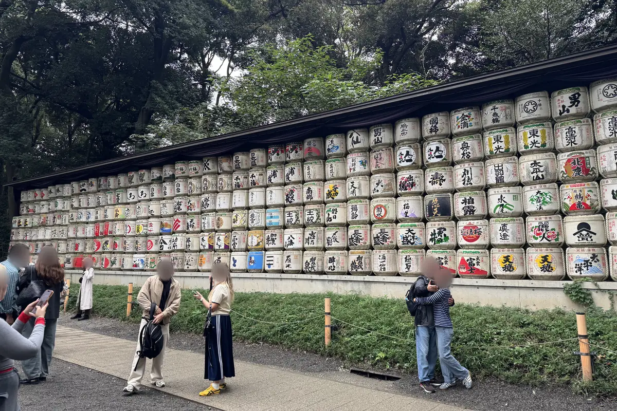 Botti di sakè impilate a lato del viale. Le botti, con le scritte e i disegni delle marche, sono allineate sotto una tettoia su più livelli, in una lunga fila orizzontale.