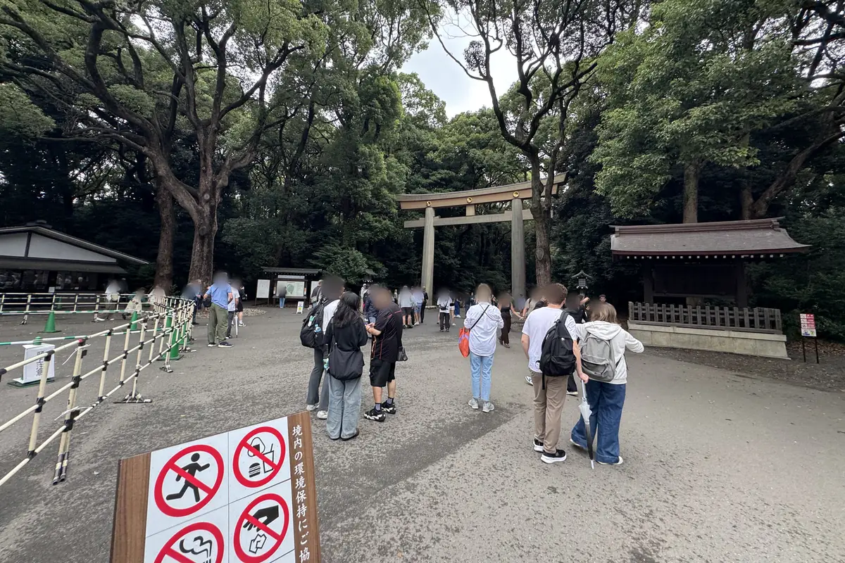 L'ingresso Harajuku del Meiji Jingu. In fondo al piazzale, dove comincia la foresta, si erge un grande torii di legno. In primo piano c'è un cartello che mostra con dei disegni i divieti in vigore nell'area del santuario.