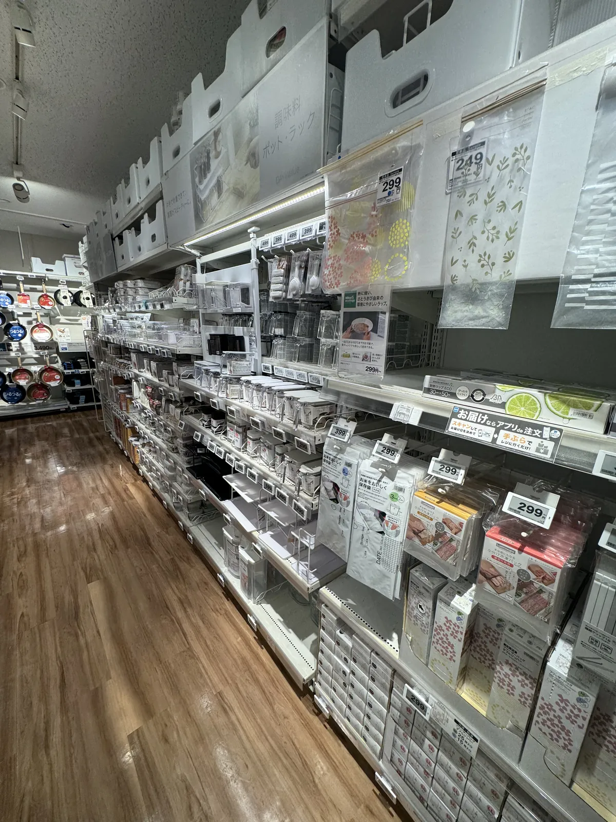 厨房用品卖场的通道。右侧货架上摆放着透明的保鲜盒和调味料容器,里面挂着平底锅。