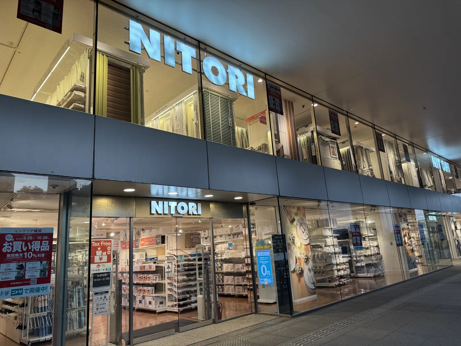 从街上看到的宜得利门店正面。玻璃墙上方有大大的“NITORI”字样,从上面楼层的窗户可以看到窗帘卖场。入口左侧有红色的“Tax Free”牌子,以及标示营业时间“10:00~21:00”的牌子。
