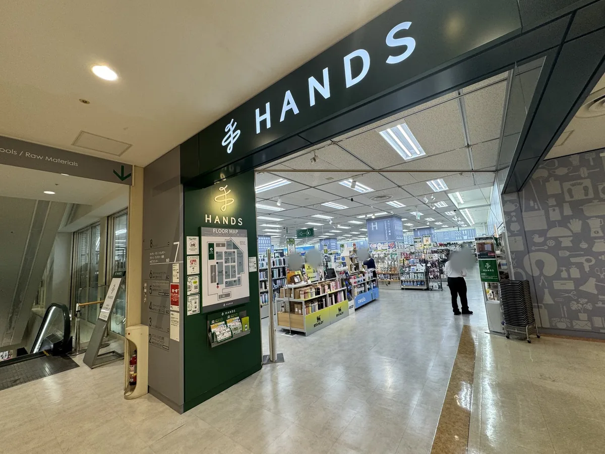 Ingresso di HANDS Shinjuku. Sull'insegna verde c'è la scritta «HANDS» in lettere bianche e sulla colonna ci sono la mappa dei piani e le indicazioni dei reparti di ogni piano.