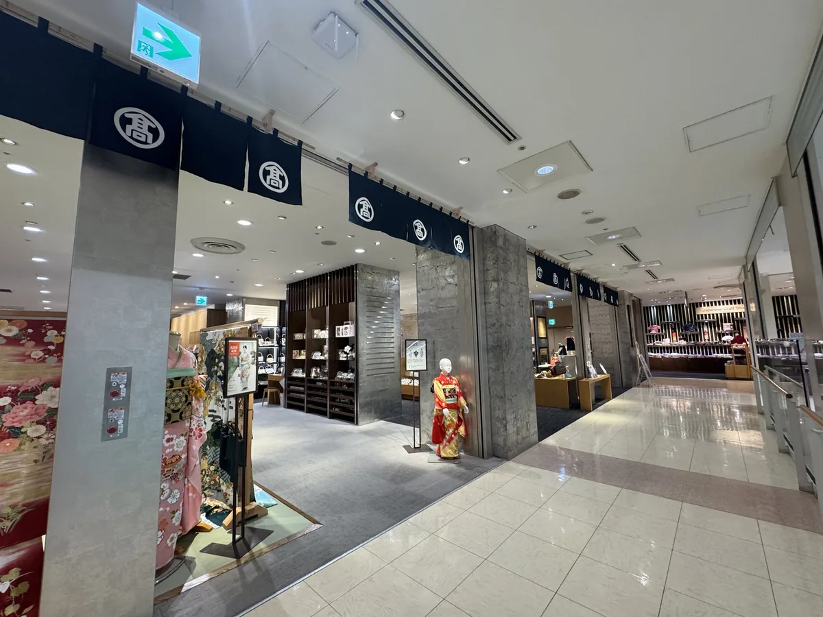 Ingresso del reparto kimono. È appesa una tenda noren blu scuro con lo stemma di Takashimaya (il carattere 高 dentro un cerchio) e c'è un manichino vestito con un furisode.